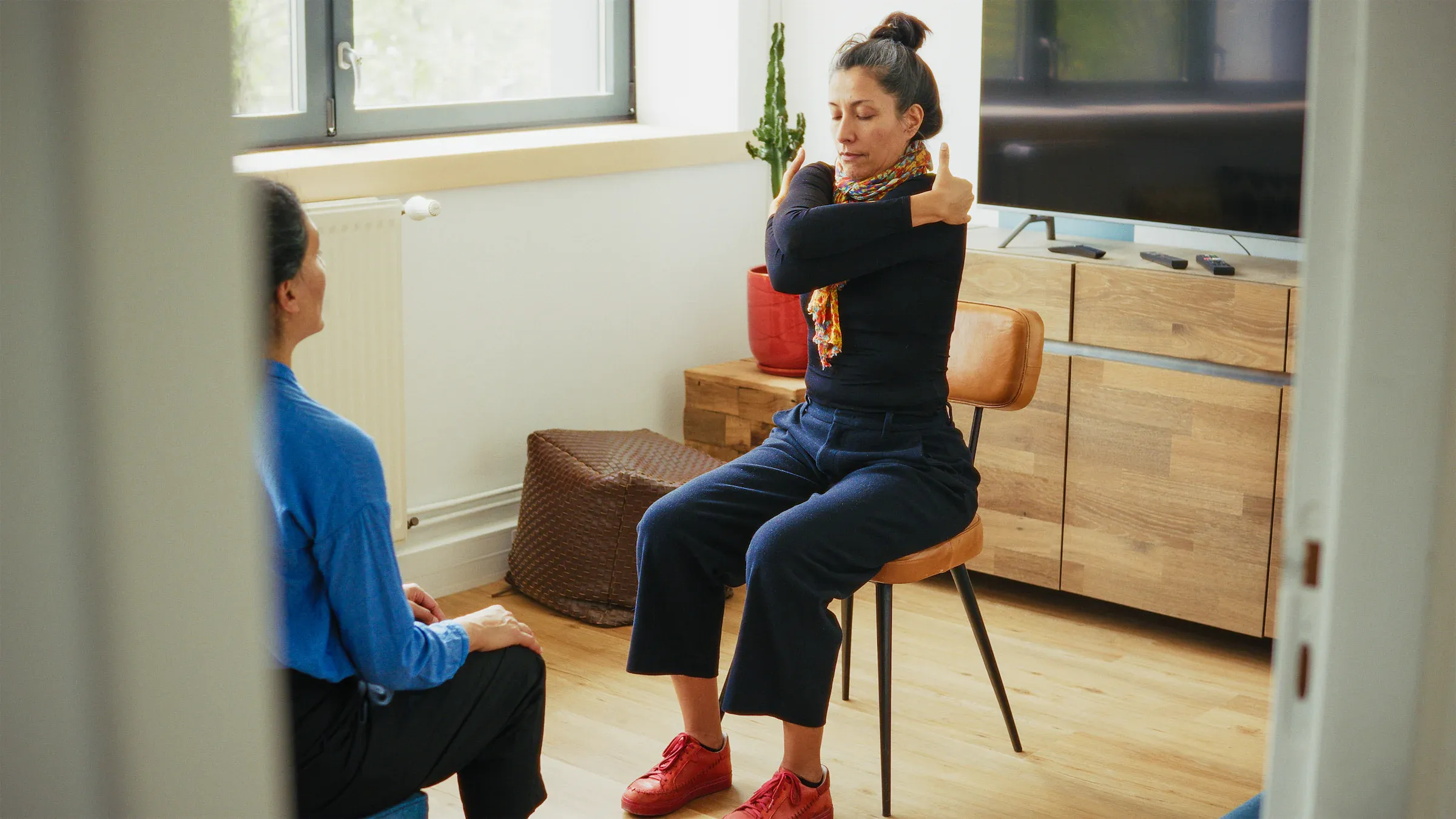 A woman seated in a calm living room during a filmed conversation.