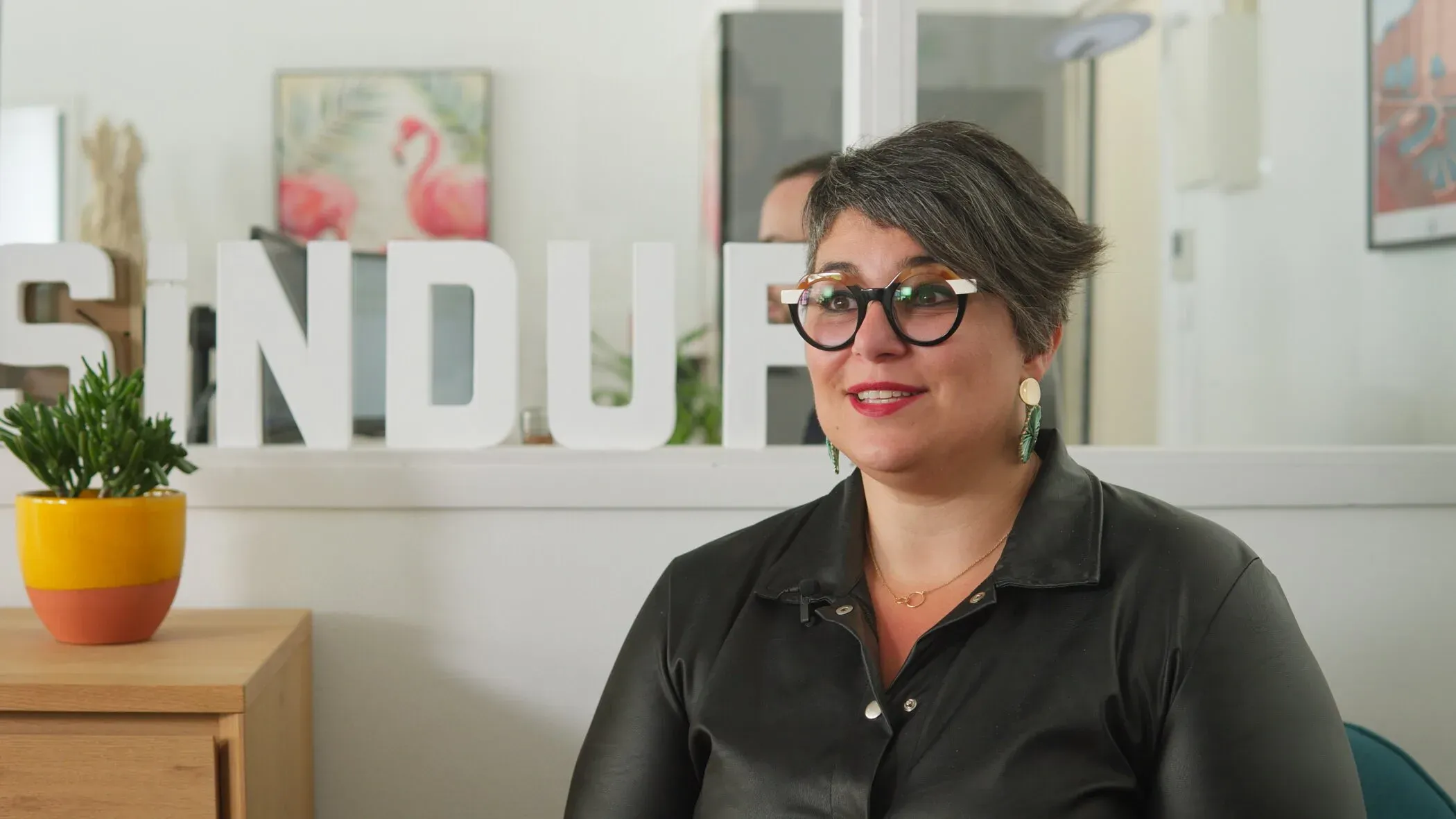 A woman with glasses in an office setting during the Sindup production.